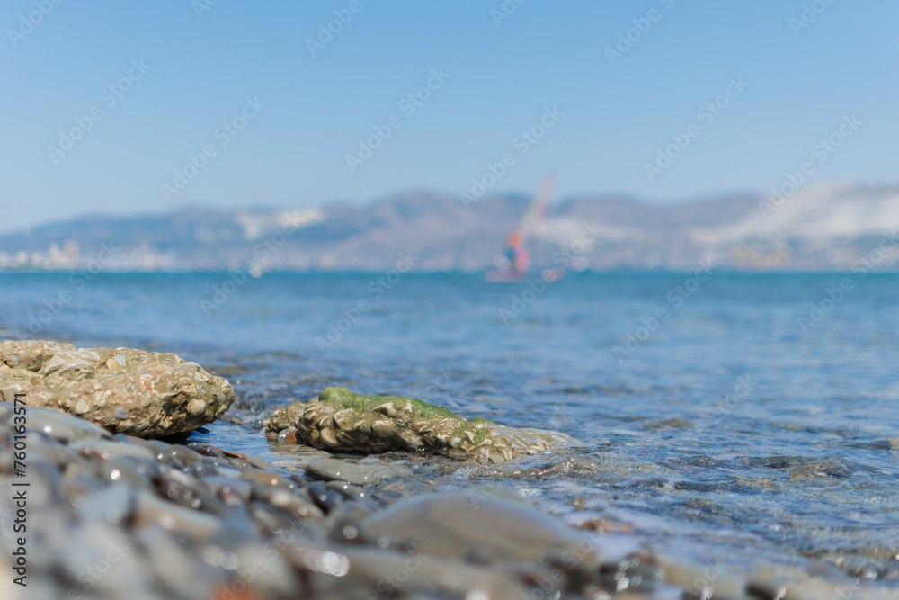 Seascape - wet round pebbles in the foreground are covered with a wave of the blue sea, mountain hills are visible in the distance on the horizon