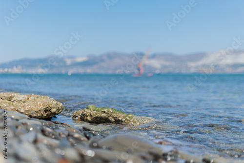 Seascape - wet round pebbles in the foreground are covered with a wave of the blue sea, mountain hills are visible in the distance on the horizon