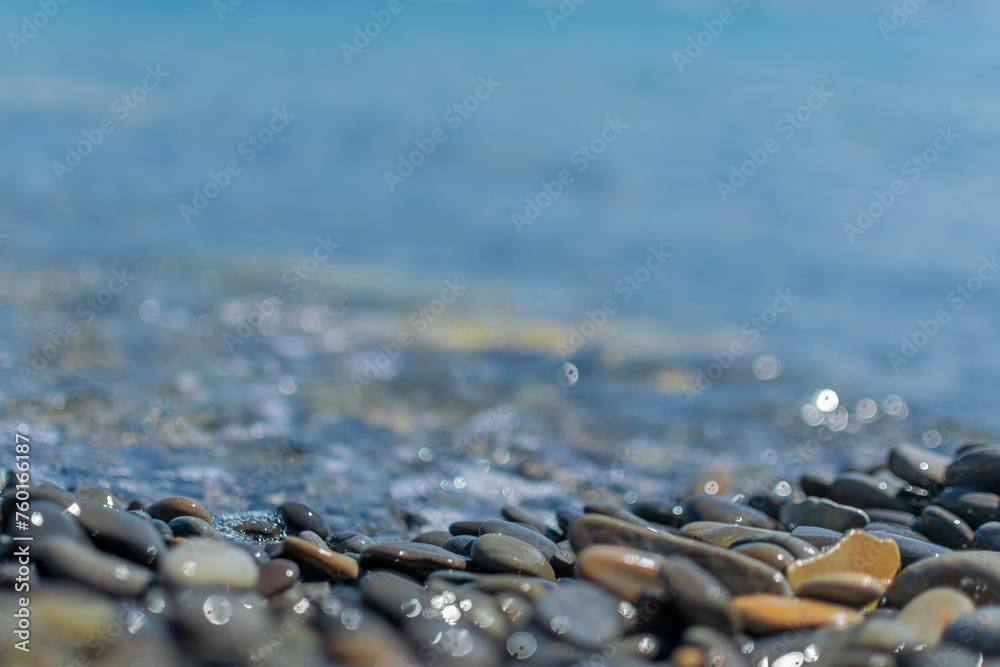 Wet round pebble stones in the foreground are covered by a wave of the blue sea