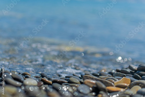 Obraz na płótnie Wet round pebble stones in the foreground are covered by a wave of the blue sea w salonie