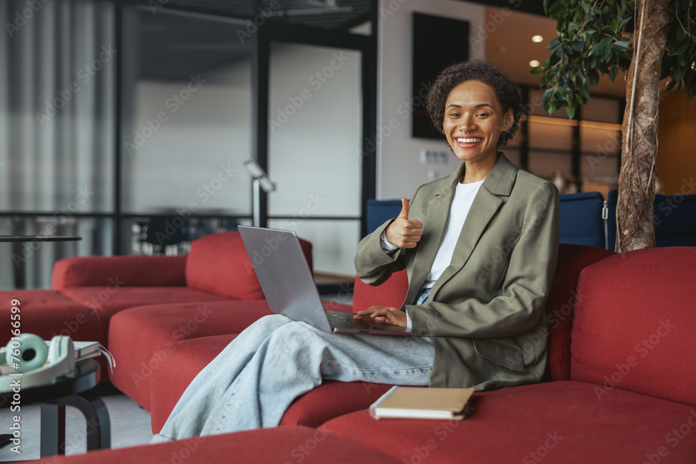 a woman is sitting on a red couch with a laptop and giving a thumbs up in nice modern coworking office a woman is sitting on a red couch with a laptop and giving a thumbs up in nice modern coworking office