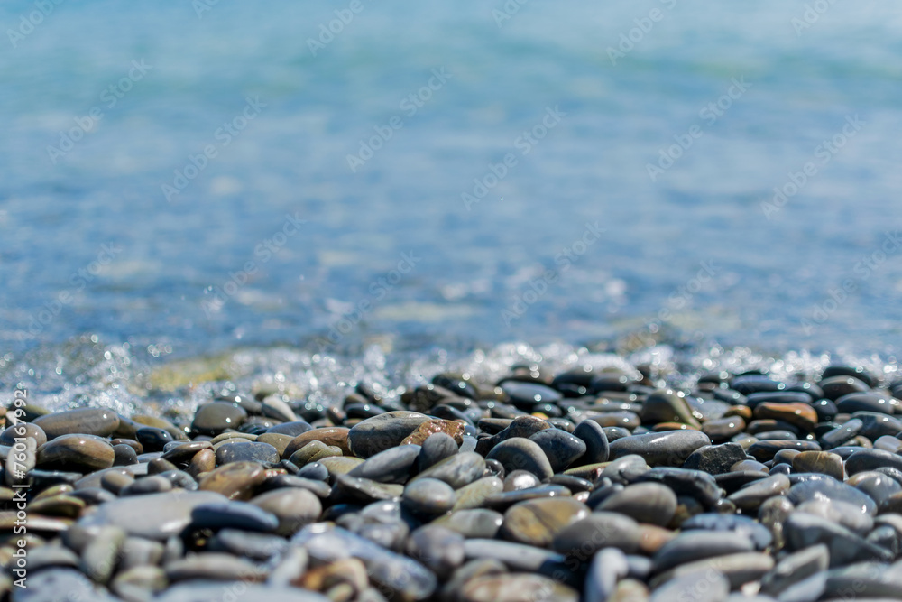 Wet round pebble stones in the foreground are covered by a wave of the blue sea