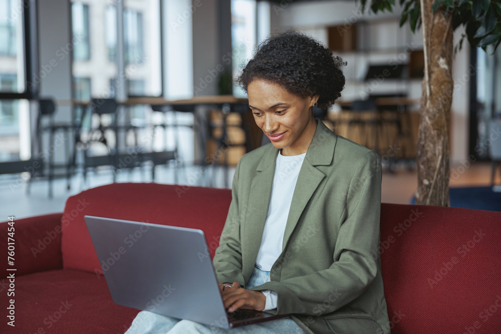 Woman in formal wear sitting on red couch using a laptop computer Woman in formal wear sitting on red couch using a laptop computer