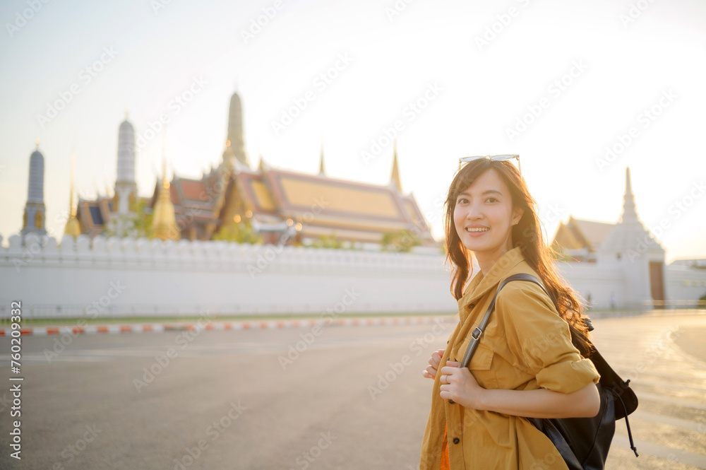 Traveler asian woman in her 30s, backpack slung over her shoulder, explores the intricate details of Wat Pra Kaew with childlike wonder. Sunlight dances on the golden rooftops.