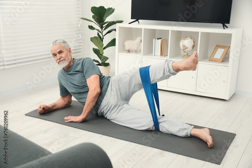 Senior man doing exercise with fitness elastic band on mat at home photo