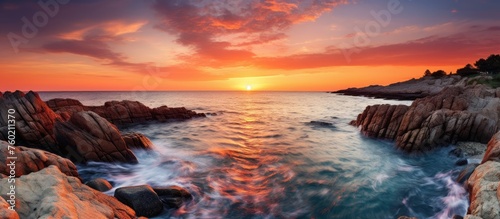 Majestic Sunset Casting Warm Glow Over Tranquil Ocean with Coastal Rocks