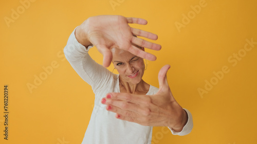 Young hairless woman shows compositional gesture, winks, isolated on yellow background in studio