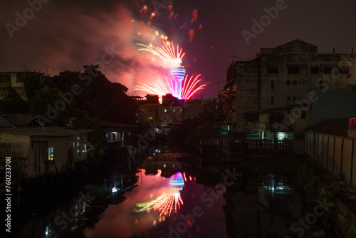 Fireworks celebration at Samut Prakan Observation Tower with river reflection in urban city town, Thailand.