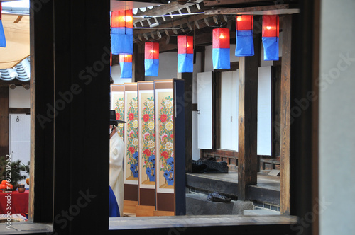 Unidentified old Korean noble man wears a black traditional hat and stands in front of traditional drawing wall room dividers in old traditional Hanok house village.