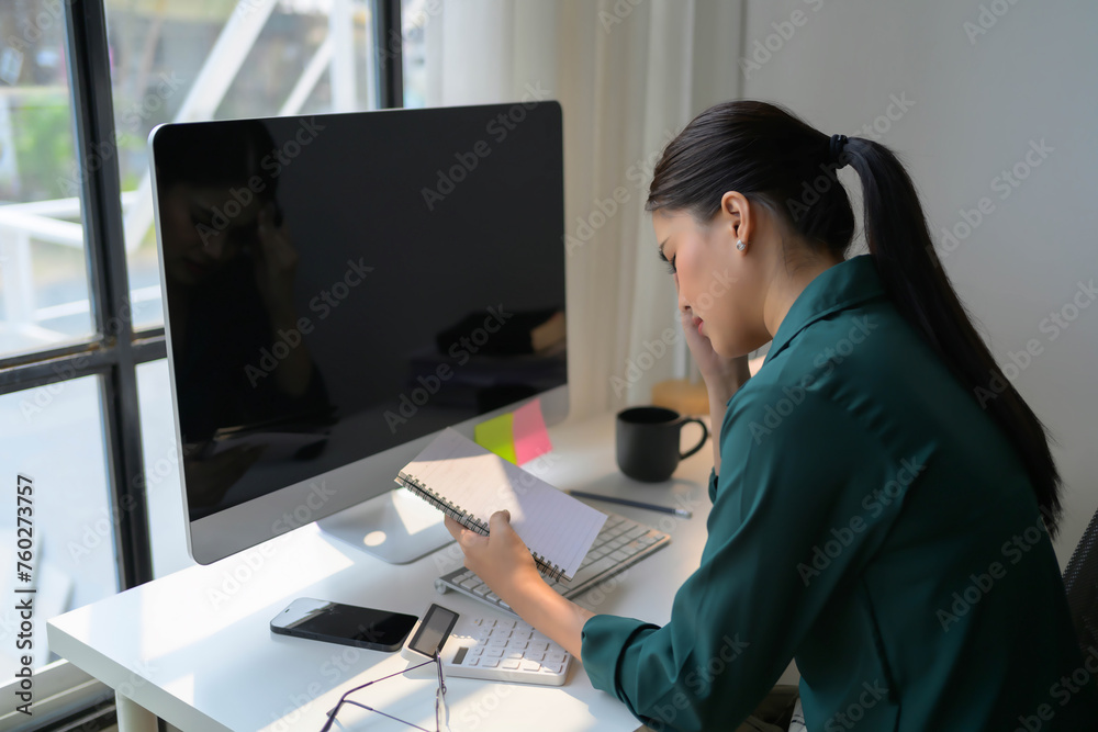 A woman is sitting at a desk with a computer monitor and a notebook A woman is sitting at a desk with a computer monitor and a notebook