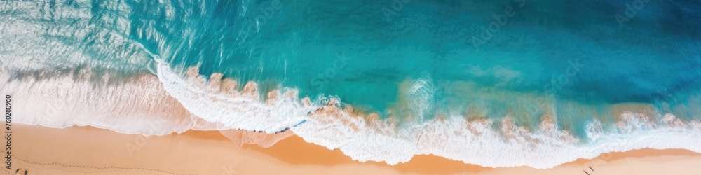 Aerial view of a paradise beach where the waves of the sea break on the shore. Top view of a sandy coast with turquoise blue water and white foam on sunny day. Summertime, marine, seashore banner. 