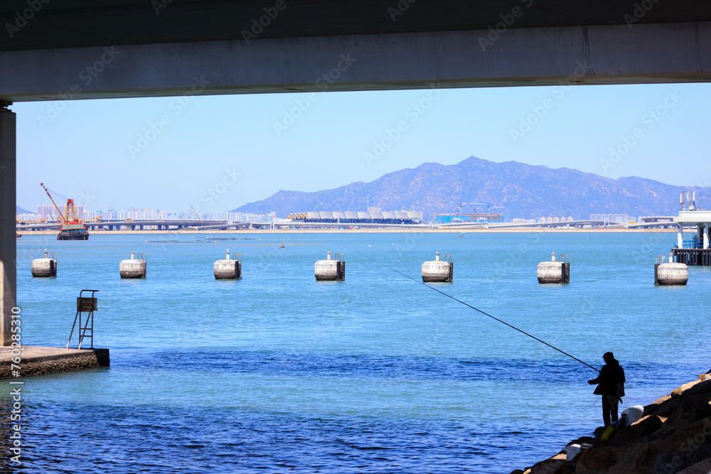 Solitude by the Sea: A Fisherman’s Quiet Contemplation Under the Bridge