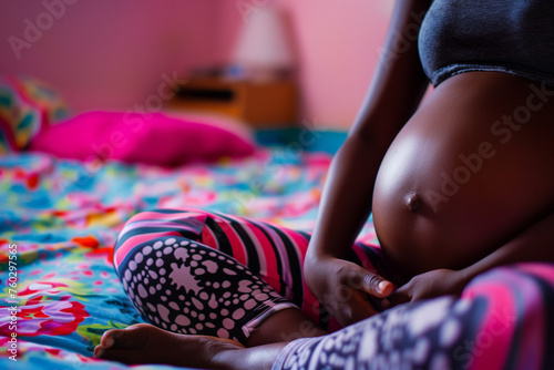 anonymous black woman's pregnant torso sitting on bed, colorful pattern clothes
