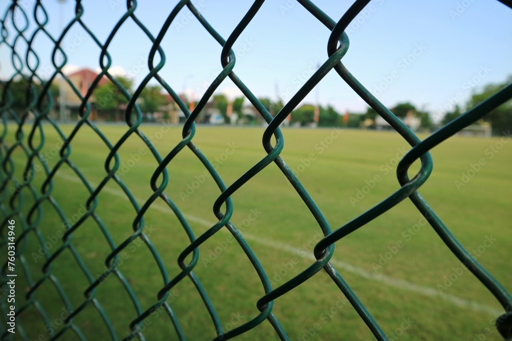 Fototapeta premium Green soccer field inside the green fence with morning sunlight.