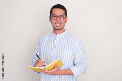 Adult Asian man smiling at the camera while writting something on the book photo