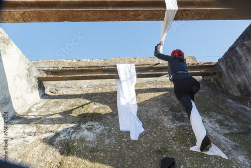 Mujer que sube una pared con tela blanca por encima de una biga de hierro
