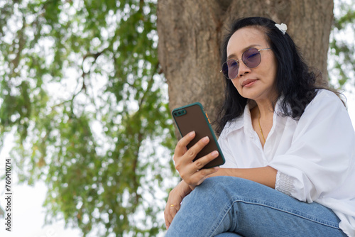 Happy senior Asian woman text messaging or using mobile phone while relaxing