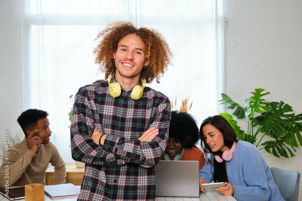 Young Latin man smiling and looking at camera with his college mates studying in the background.