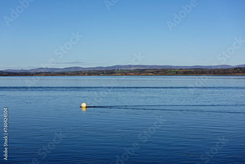 A faded yellow mooring buoy being pushed by the strong currents of the tidal flow within the Montrose Basin on a bright March Morning.