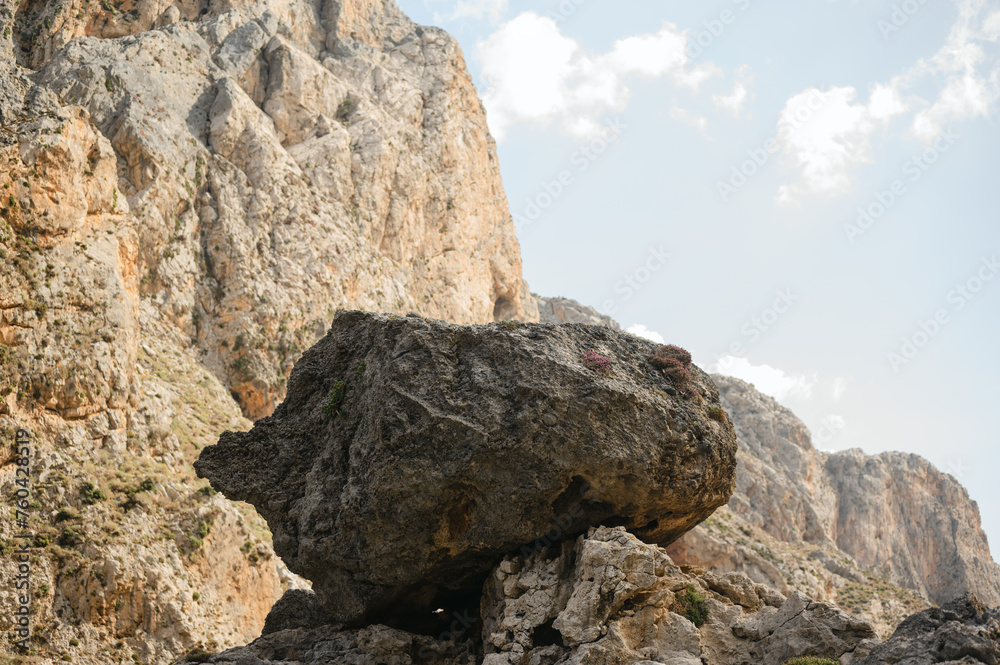 Large boulder amidst rugged cliffside and blue sky in Crete