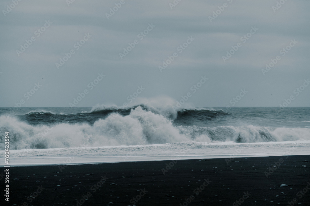 Waves crash against contrast black sand rock beach Icelandic nature