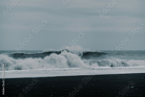 Waves crash against contrast black sand rock beach Icelandic nature © Cavan