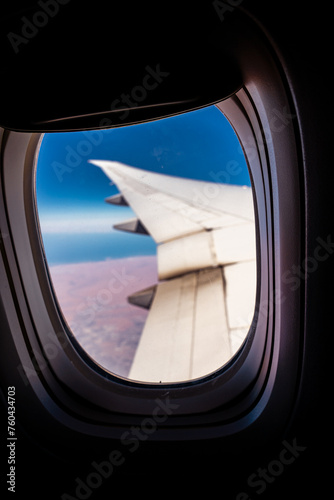 Aerial view of clouds and blue sky from window of airplane.   Airplane wing against the blue sky from the porthole.  © Strikernia