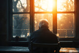 Elderly man sitting alone facing window light