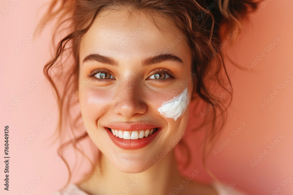 Fototapeta premium Beautiful smiling young woman spreads anti-aging cream on her face