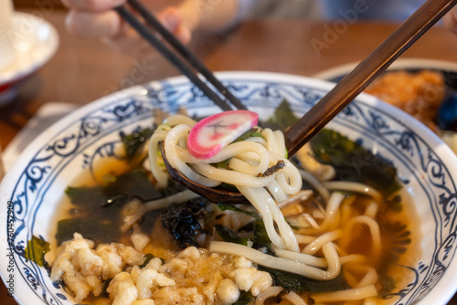 Closeup photo of Udon (Japanease noodle) held in a chopsticks, taken at a restaurant
