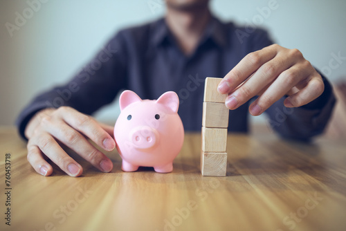 Person building a tower from wooden blocks beside a piggy bank, symbolizing financial planning and saving