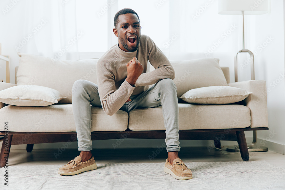 Relaxed African American man sitting on a comfortable sofa in his modern living room, lost in deep thought His smiling face and relaxed posture convey a sense of contentment and happiness, while the