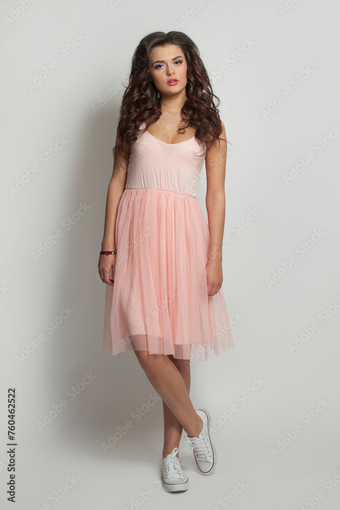 Perfect fashion model woman in pink dress and white shoes on feet standing against white studio wall background Perfect fashion model woman in pink dress and white shoes on feet standing against white studio wall background
