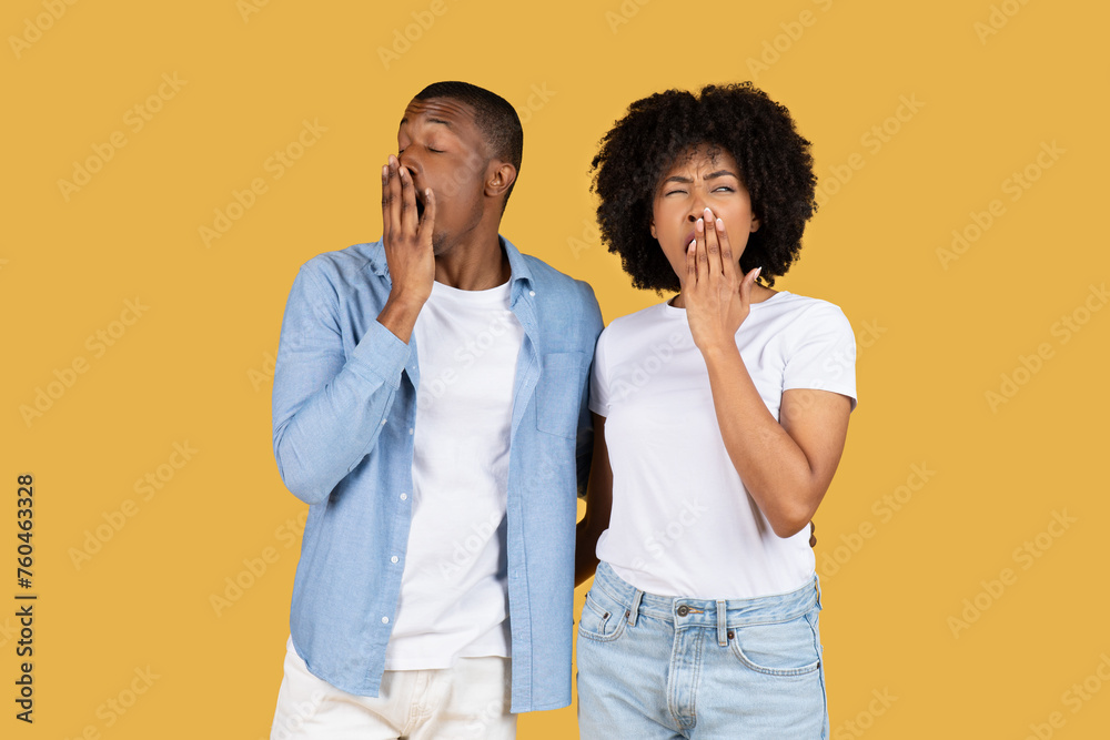 A young couple in casual clothes looking tired and bored, yawning with hands over their mouths A young couple in casual clothes looking tired and bored, yawning with hands over their mouths