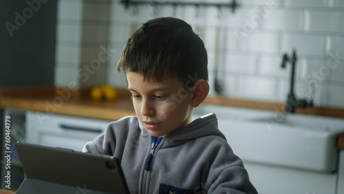 Photography Cute kid sit in the kitchen playing mobile game on digital tablet device