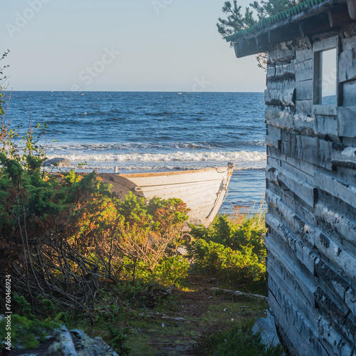 an ancient Pomeranian hut on the seashore against the background of the sea and the blue sky and the bow of a wooden longboat photo