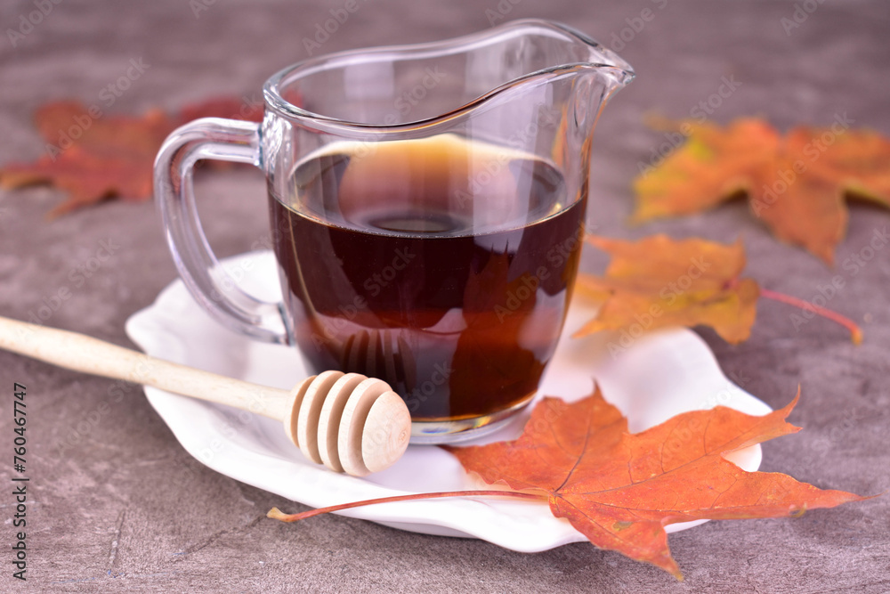 Sweet maple syrup in a transparent gravy boat on a gray background.
