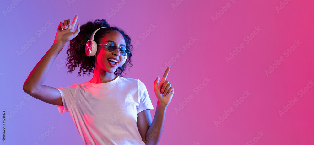 Joyful black woman with sunglasses and headphones dancing on neon background, free space - obrazy, fototapety, plakaty 