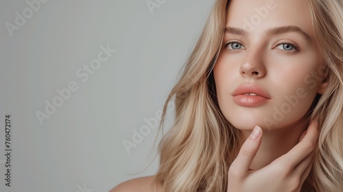 Radiant blonde model gently caresses her flawless complexion, showcasing a natural makeup look on a sleek studio background with copy space.