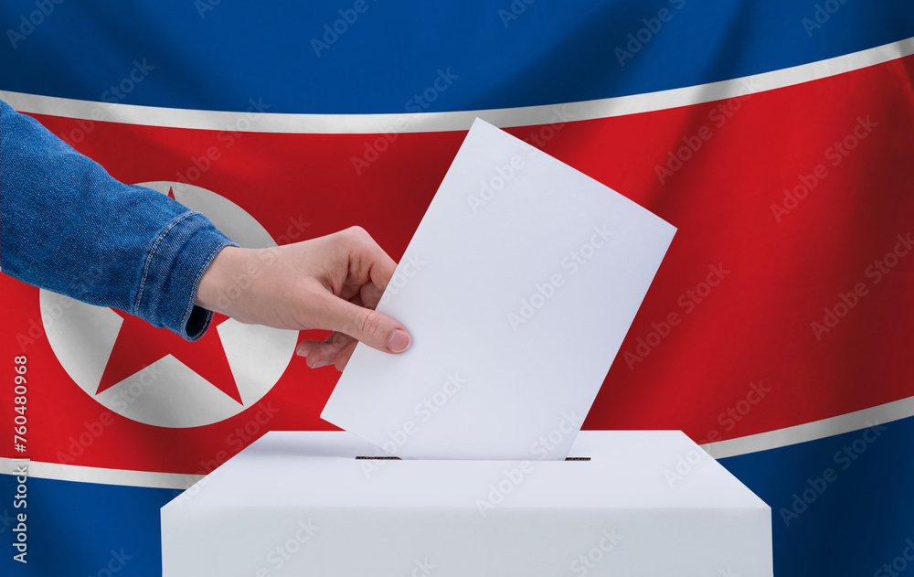 Elections in North Korea. The concept of voting. A hand throws a ballot into the ballot box. The flag of North Korea on the background. Elections in North Korea. The concept of voting. A hand throws a ballot into the ballot box. The flag of North Korea on the background.