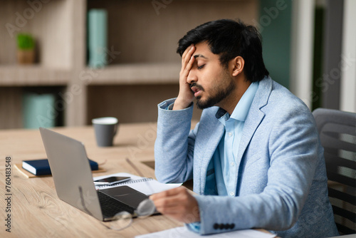 Exhausted Middle Eastern Businessman Touching Face Sitting At Laptop Indoor