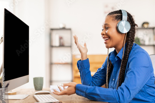 Joyful black female student with headphones studying at home