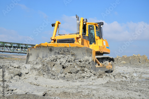 The crawler bulldozer against the background of a huge bucket excavator in the Brown Coal Mine. Heavy industry. Heavy onstruction equipment. photo
