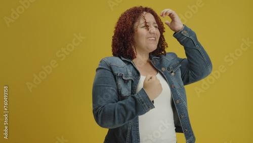 Smiling overjoyed hispanic young woman in denin jacket posing doing winner gesture, say Yes isolated on yellow background in studio. People sincere emotions, lifestyle concept
 photo