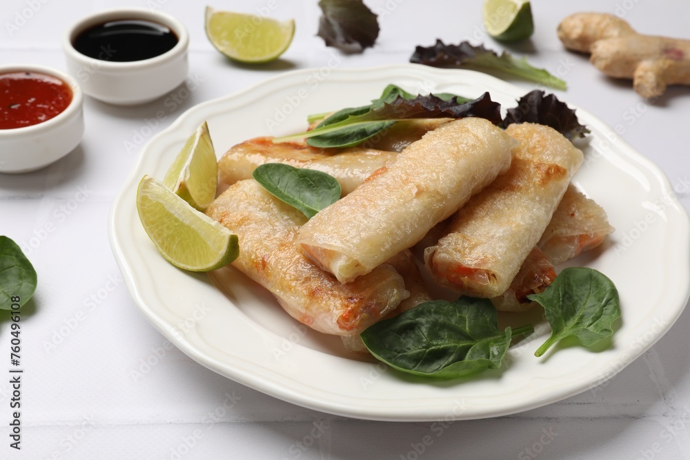 Plate with tasty fried spring rolls and spinach on white tiled table, closeup Plate with tasty fried spring rolls and spinach on white tiled table, closeup
