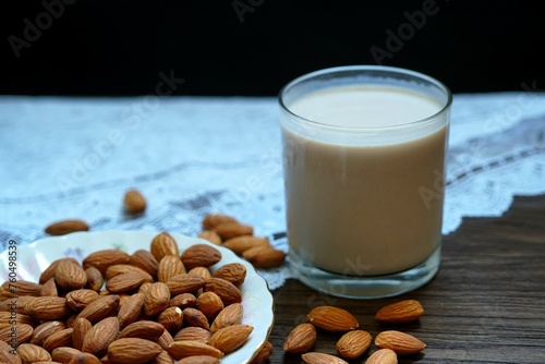 A glass of almond milk with almonds on a white plate and a wooden table