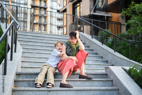 Happy family: mother and child son hugging and laugh sitting on the city stairs. motherhood concept, togetherness, love emotion. Urban city concept, residential complex in Ukraine. High quality photo
