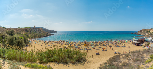Mellieha, Malta - October 1st 2018: Sunbathers on the beach at Golden Bay which was formerly called Military Bay. Above the cliffs in the background is Ghajn Tuffieha Tower. photo