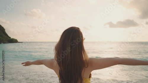 Rear view Asian young women raises arms into air while open arms enjoying the view on the beach. Summer vacation at sea for a happy female. 28 yearold woman who is carefree and freedom. slow motion photo