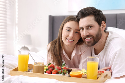 Family portrait of happy couple with tray of tasty breakfast on bed at home. Space for text